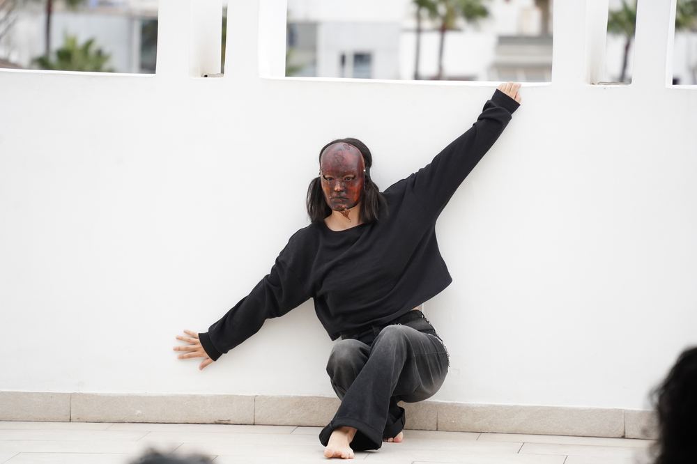 Masked dancer performing against a white wall